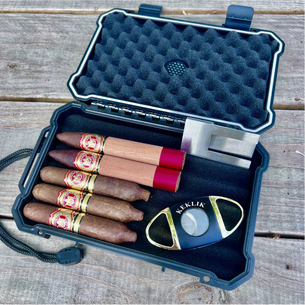 Open black hard-shell travel case with five bundled cigars and a stainless steel cutter resting on a weathered wood plank surface, the starter kit every cigar accessories guide should cover