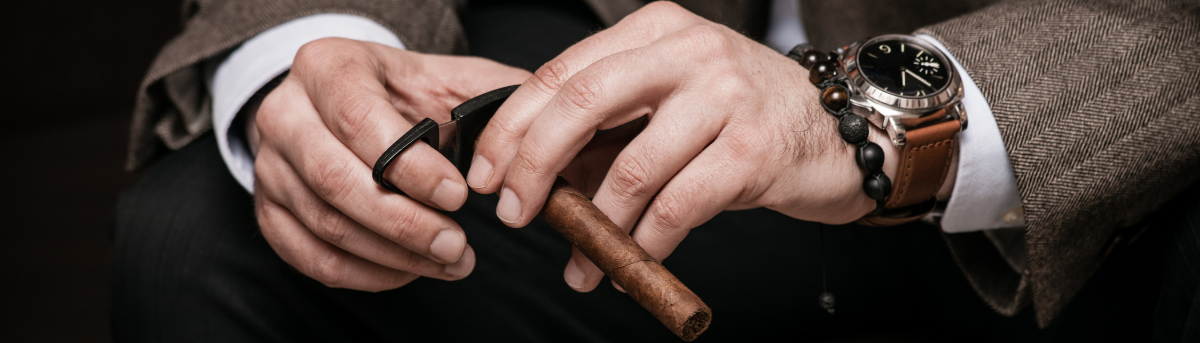 Close-up of a person's hands holding a cigar with a watch on the wrist, dressed in formal attire.